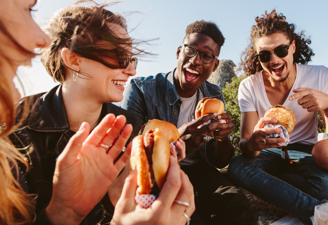 A group of people sitting outside eating hamburgers.