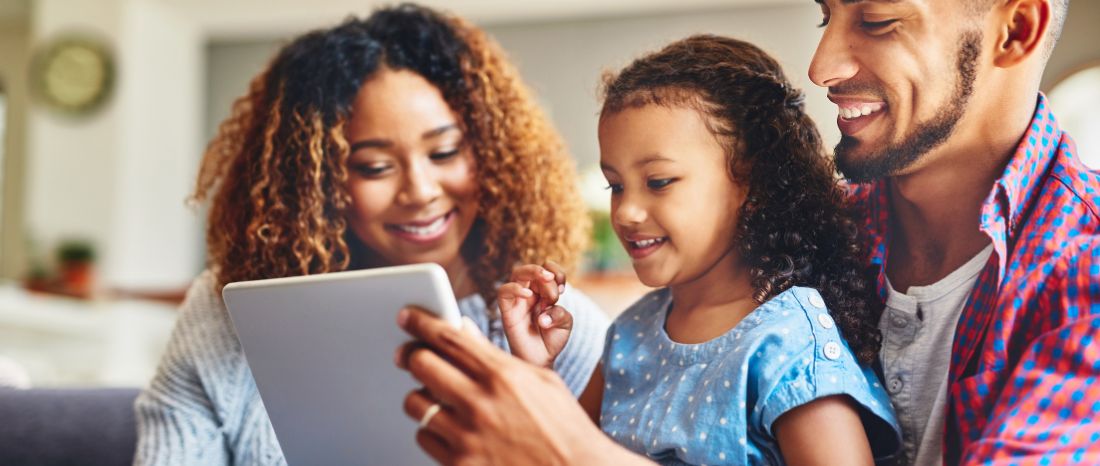 A couple and their daughter sitting together, using a tablet.
